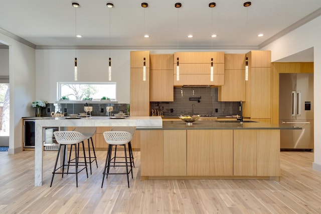 kitchen with a large island with sink, high end fridge, pendant lighting, and light brown cabinets