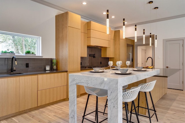 kitchen with sink, light wood-type flooring, light brown cabinetry, and an island with sink