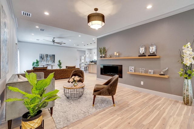 living room featuring ceiling fan, light hardwood / wood-style floors, and crown molding