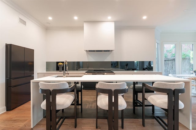 kitchen with sink, black fridge, light hardwood / wood-style floors, and ornamental molding