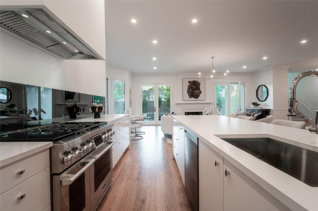 kitchen with sink, white cabinets, light hardwood / wood-style flooring, wall chimney range hood, and appliances with stainless steel finishes