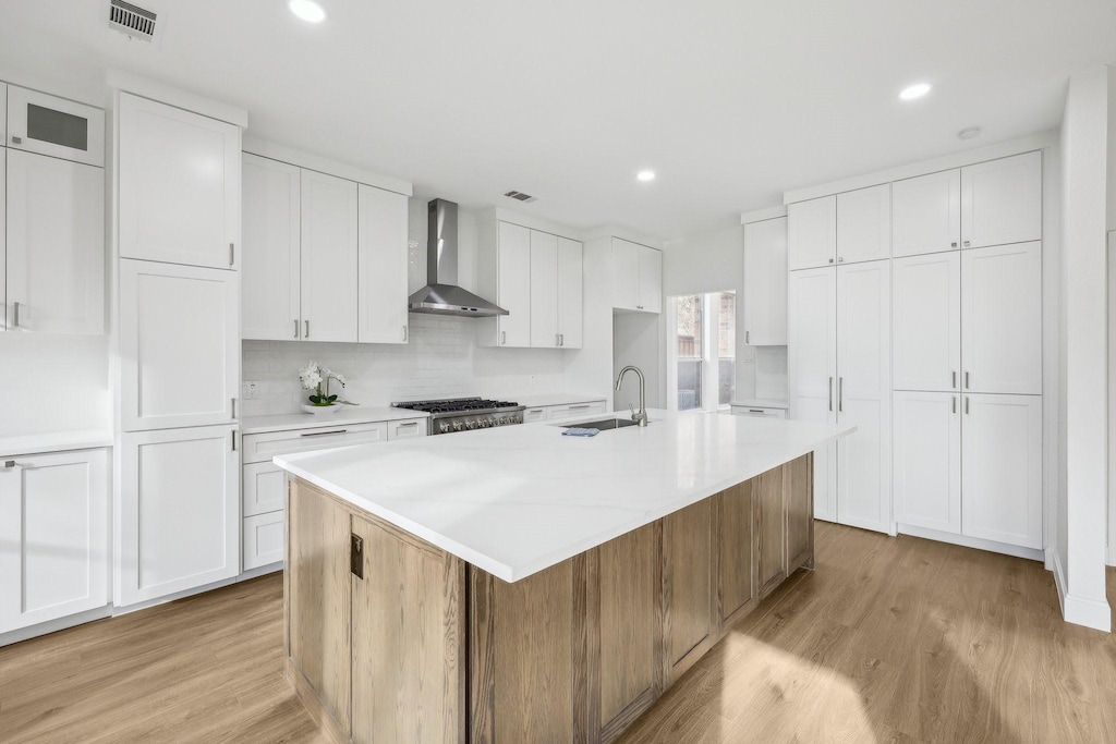 kitchen featuring a center island with sink, white cabinets, light hardwood / wood-style flooring, wall chimney range hood, and sink