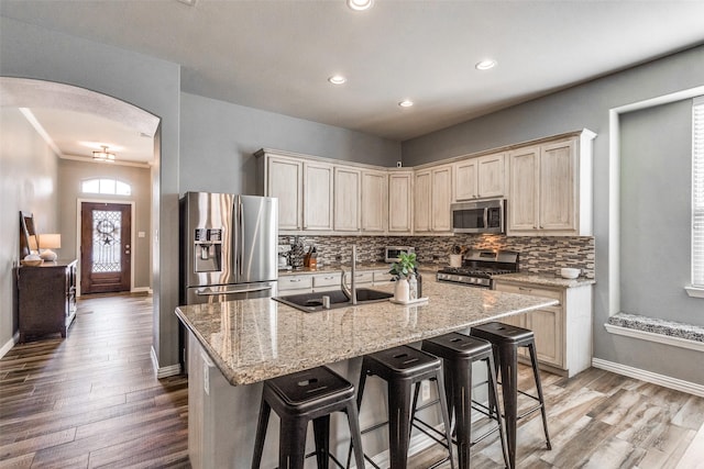 kitchen with light stone counters, a center island with sink, a breakfast bar, appliances with stainless steel finishes, and sink