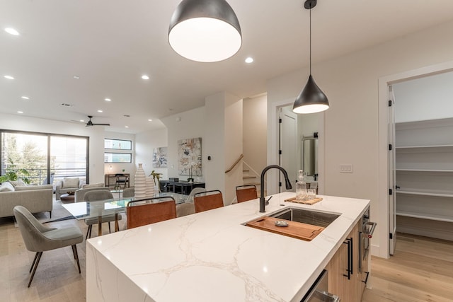 kitchen featuring sink, decorative light fixtures, ceiling fan, an island with sink, and light stone countertops