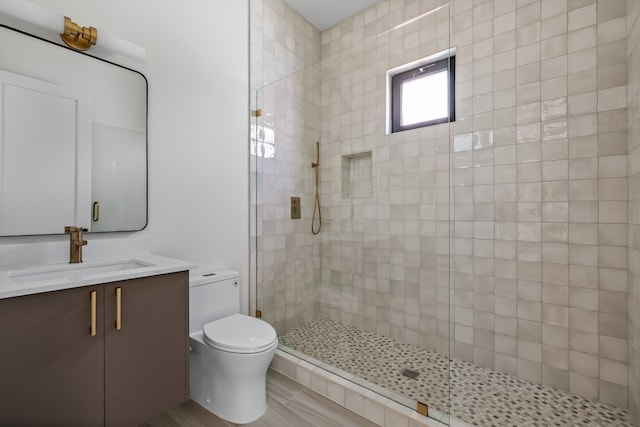 bathroom with toilet, tiled shower, and vanity