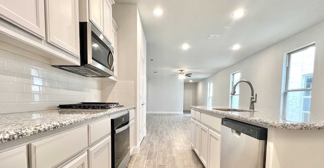 kitchen with white cabinets, stainless steel appliances, ceiling fan, light stone counters, and sink