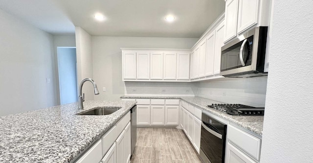 kitchen featuring stainless steel appliances, sink, white cabinetry, backsplash, and light stone countertops