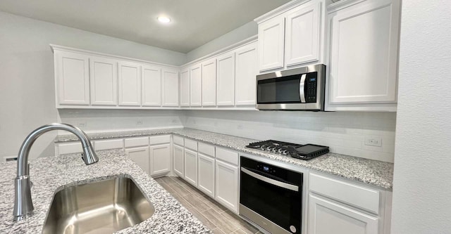 kitchen with light stone counters, appliances with stainless steel finishes, white cabinetry, and sink