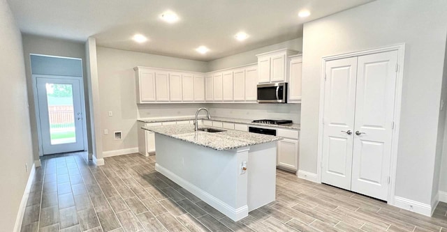 kitchen featuring a center island with sink, light stone counters, sink, white cabinetry, and black gas stovetop