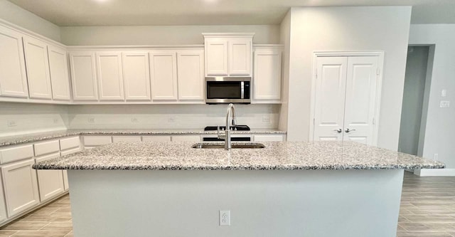 kitchen with light stone countertops, a kitchen island with sink, white cabinetry, and sink