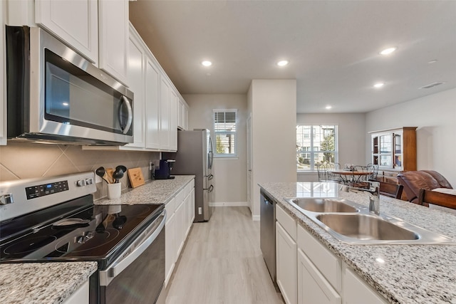 kitchen with sink, white cabinetry, tasteful backsplash, light wood-type flooring, and appliances with stainless steel finishes