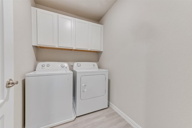 laundry area with cabinets, washing machine and dryer, and light hardwood / wood-style floors