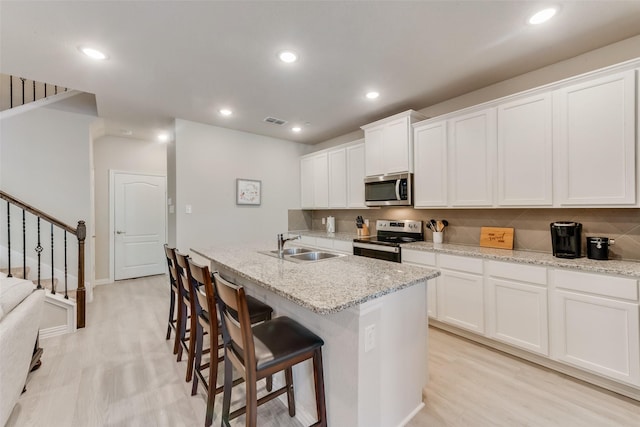 kitchen featuring appliances with stainless steel finishes, light stone countertops, a center island with sink, and white cabinets