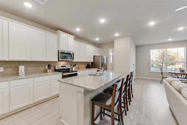 kitchen with sink, stainless steel appliances, white cabinets, and a center island with sink