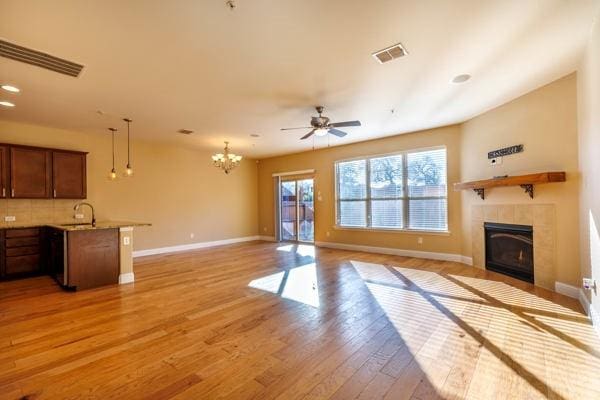 unfurnished living room with light wood-type flooring, a fireplace, sink, and ceiling fan with notable chandelier