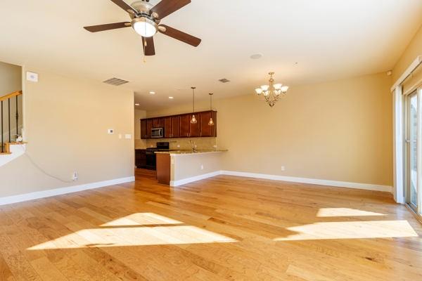 unfurnished living room with ceiling fan with notable chandelier and light hardwood / wood-style flooring