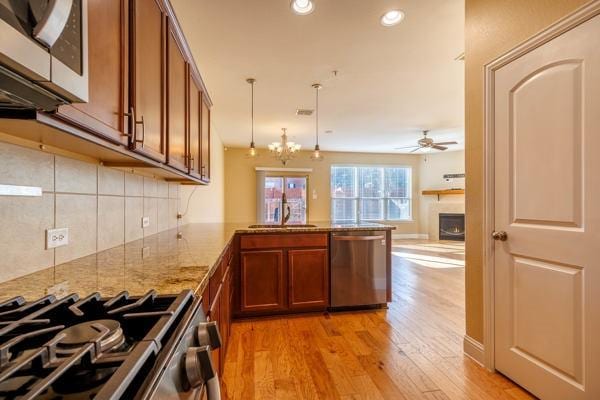 kitchen with ceiling fan with notable chandelier, hanging light fixtures, appliances with stainless steel finishes, and kitchen peninsula