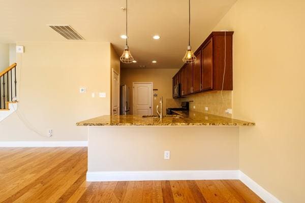 kitchen with decorative backsplash, pendant lighting, kitchen peninsula, and light stone countertops