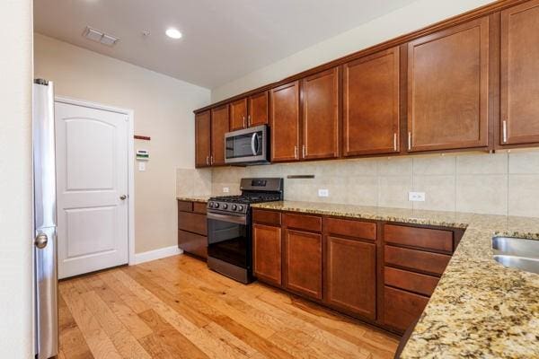 kitchen with decorative backsplash, light stone countertops, appliances with stainless steel finishes, and light hardwood / wood-style flooring