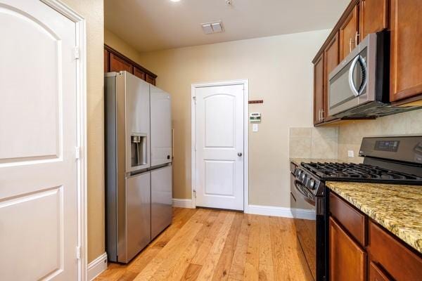 kitchen with light stone counters, light hardwood / wood-style floors, backsplash, and appliances with stainless steel finishes