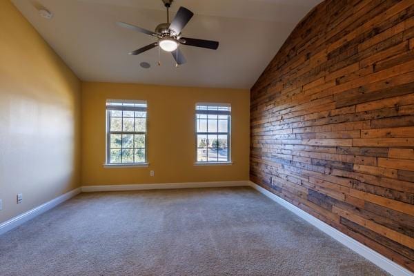 carpeted spare room featuring ceiling fan, wood walls, and vaulted ceiling