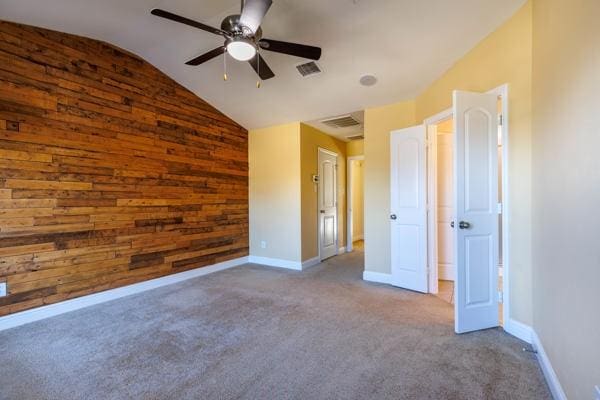 carpeted empty room featuring ceiling fan, lofted ceiling, and wooden walls