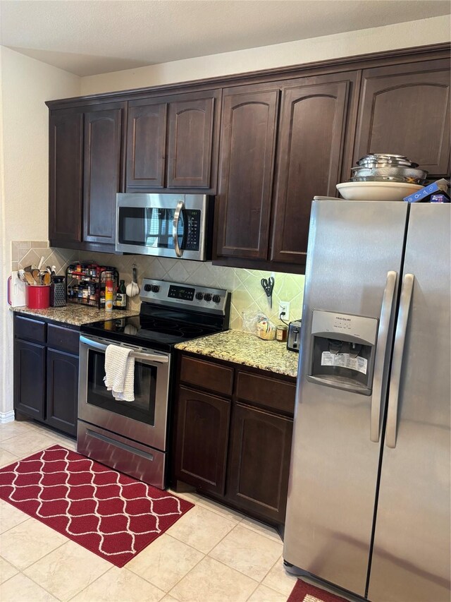 kitchen with light tile patterned floors, appliances with stainless steel finishes, decorative backsplash, light stone countertops, and dark brown cabinetry