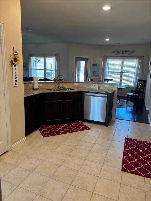 kitchen with light stone countertops, sink, kitchen peninsula, light tile patterned flooring, and stainless steel dishwasher