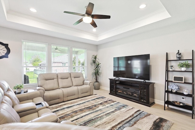 living room with a raised ceiling, ceiling fan, and light wood-type flooring