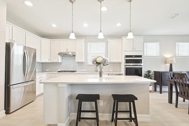 kitchen featuring light stone countertops, a center island, hanging light fixtures, stainless steel appliances, and white cabinetry