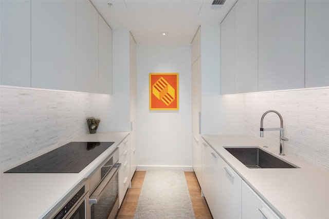 kitchen featuring black electric stovetop, tasteful backsplash, white cabinetry, and sink