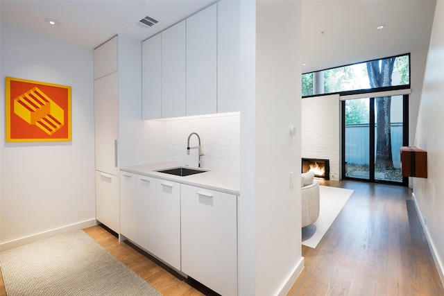 kitchen featuring sink, white cabinetry, decorative backsplash, and a fireplace