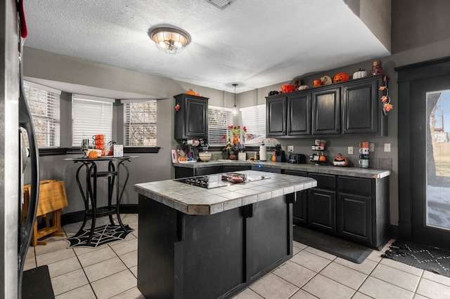 kitchen with a kitchen island, tile counters, black electric stovetop, and light tile patterned floors