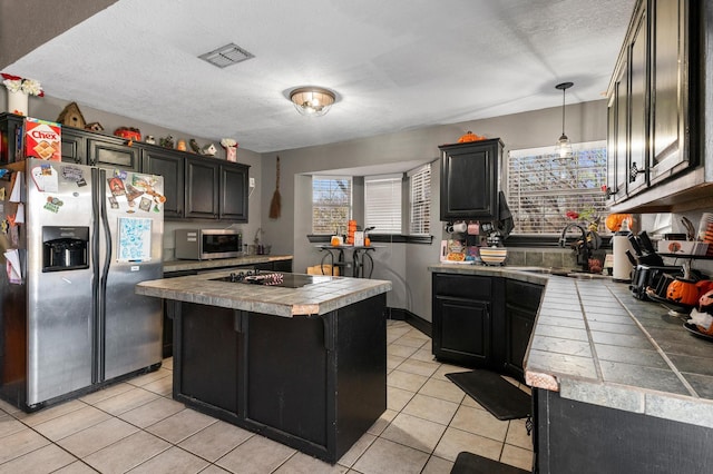 kitchen with appliances with stainless steel finishes, hanging light fixtures, a center island, tile countertops, and light tile patterned flooring