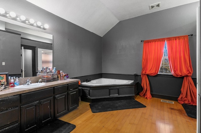 bathroom featuring a tub, vaulted ceiling, vanity, and hardwood / wood-style floors