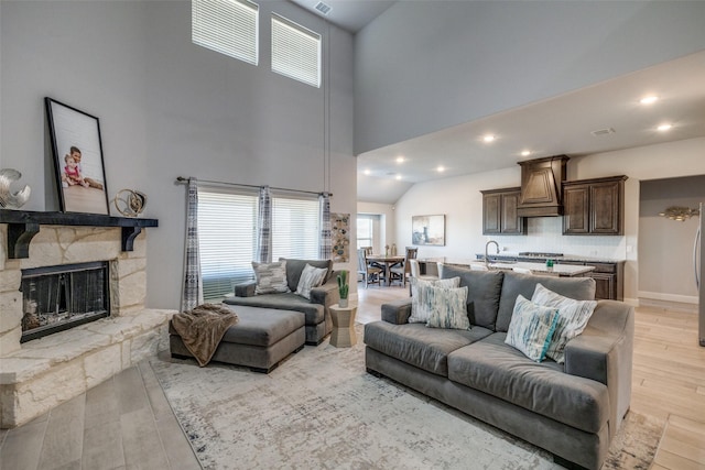 living room with light hardwood / wood-style floors, a fireplace, a towering ceiling, and sink