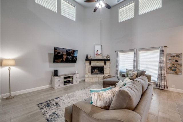 living room featuring ceiling fan, a high ceiling, wood-type flooring, and a fireplace