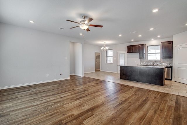 kitchen featuring tasteful backsplash, ceiling fan with notable chandelier, wood-type flooring, dark brown cabinets, and a kitchen island