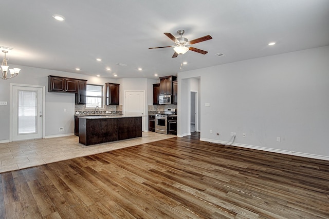 kitchen with stainless steel appliances, light hardwood / wood-style floors, ceiling fan with notable chandelier, backsplash, and dark brown cabinets