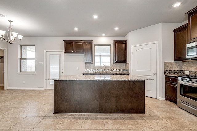 kitchen with stainless steel appliances, decorative light fixtures, light stone countertops, a kitchen island, and a notable chandelier