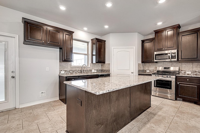 kitchen featuring light stone counters, sink, stainless steel appliances, a kitchen island, and dark brown cabinetry