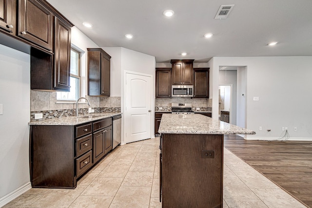 kitchen with a center island, light tile patterned floors, dark brown cabinetry, appliances with stainless steel finishes, and sink