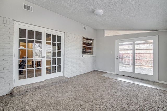 empty room featuring a textured ceiling, french doors, vaulted ceiling, and carpet flooring