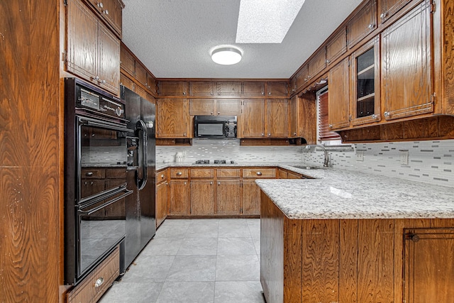 kitchen with light stone counters, kitchen peninsula, black appliances, a skylight, and sink