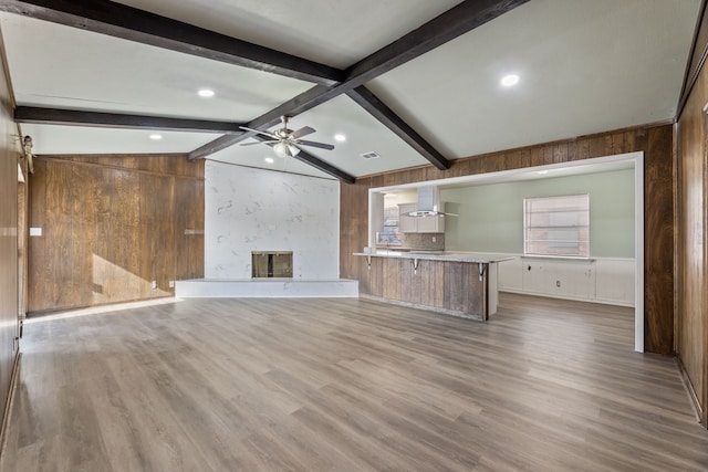 unfurnished living room with wooden walls, hardwood / wood-style floors, ceiling fan, a large fireplace, and lofted ceiling with beams