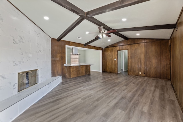 unfurnished living room featuring a tile fireplace, ceiling fan, wood-type flooring, wood walls, and lofted ceiling with beams