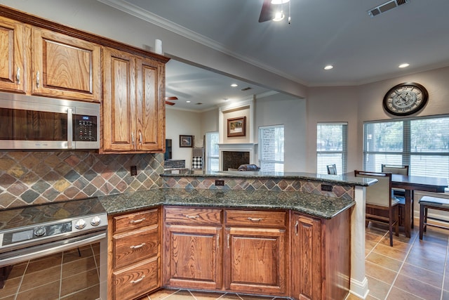 kitchen featuring dark stone countertops, appliances with stainless steel finishes, ornamental molding, light tile patterned flooring, and tasteful backsplash