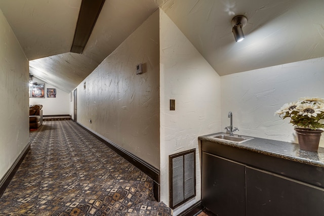 hallway with baseboards, visible vents, a textured wall, vaulted ceiling, and a sink