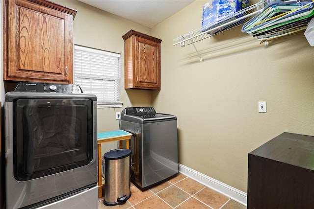 clothes washing area featuring light tile patterned floors, washing machine and dryer, cabinet space, and baseboards