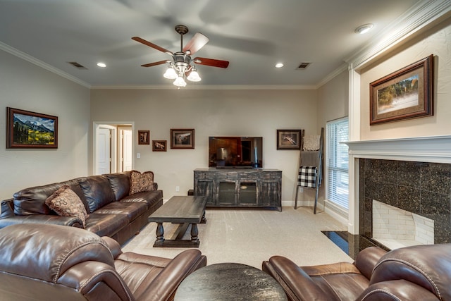 living room with a tiled fireplace, ceiling fan, crown molding, and carpet flooring